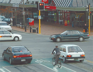 A cyclist stopped at an intersection amongst cars. 